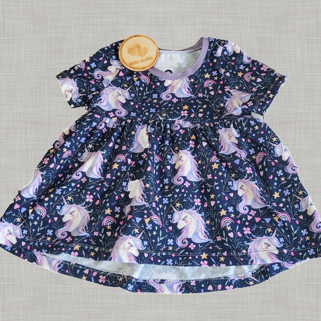 Front view of handmade children’s peplum top in unicorn fabric with Olivia’s Outfits tag, on neutral background