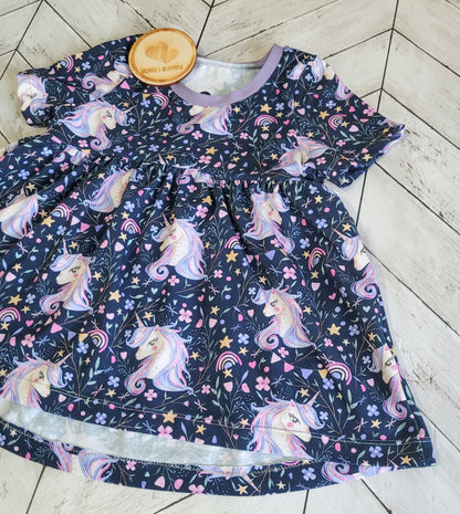 Flat lay of handmade cotton peplum top in pastel unicorn design, placed on wood floor background