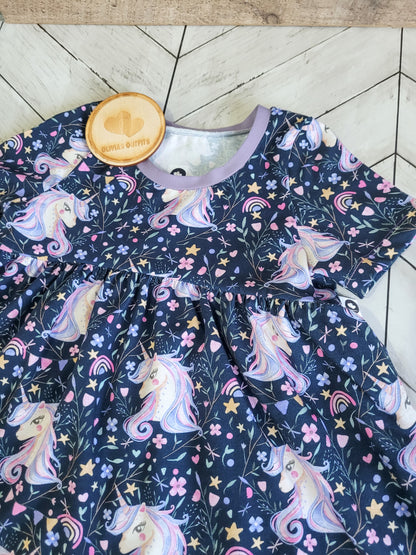 Flat lay of handmade cotton peplum top in pastel unicorn design, placed on wood floor background