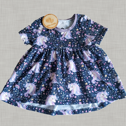 Flat lay of handmade children’s peplum top in navy unicorn print with Olivia’s Outfits logo disc